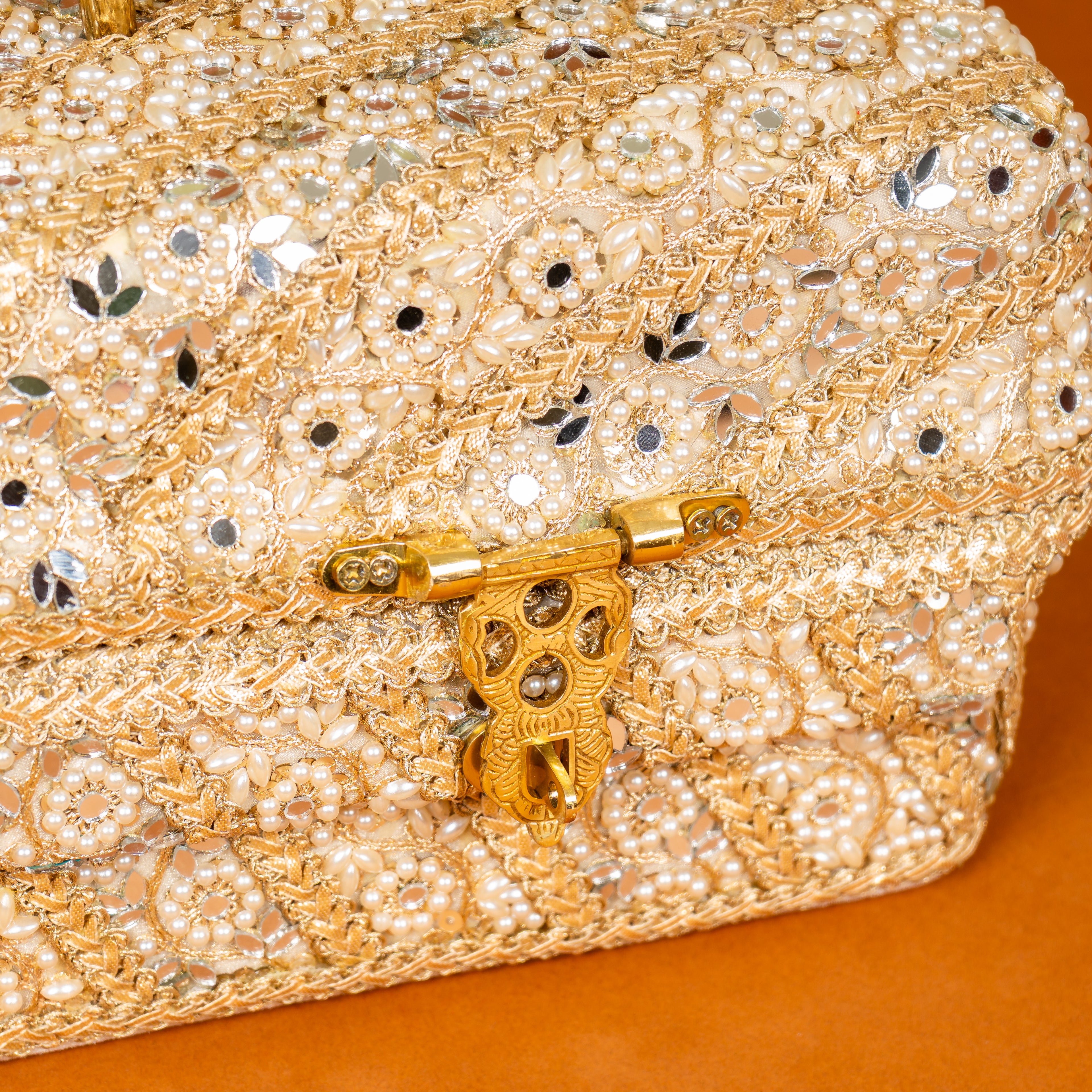 Gold beaded clutch with intricate design and decorative clasp on an orange background