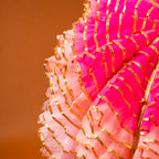 Close-up of pink and gold decorative umbrella with a blurred orange background