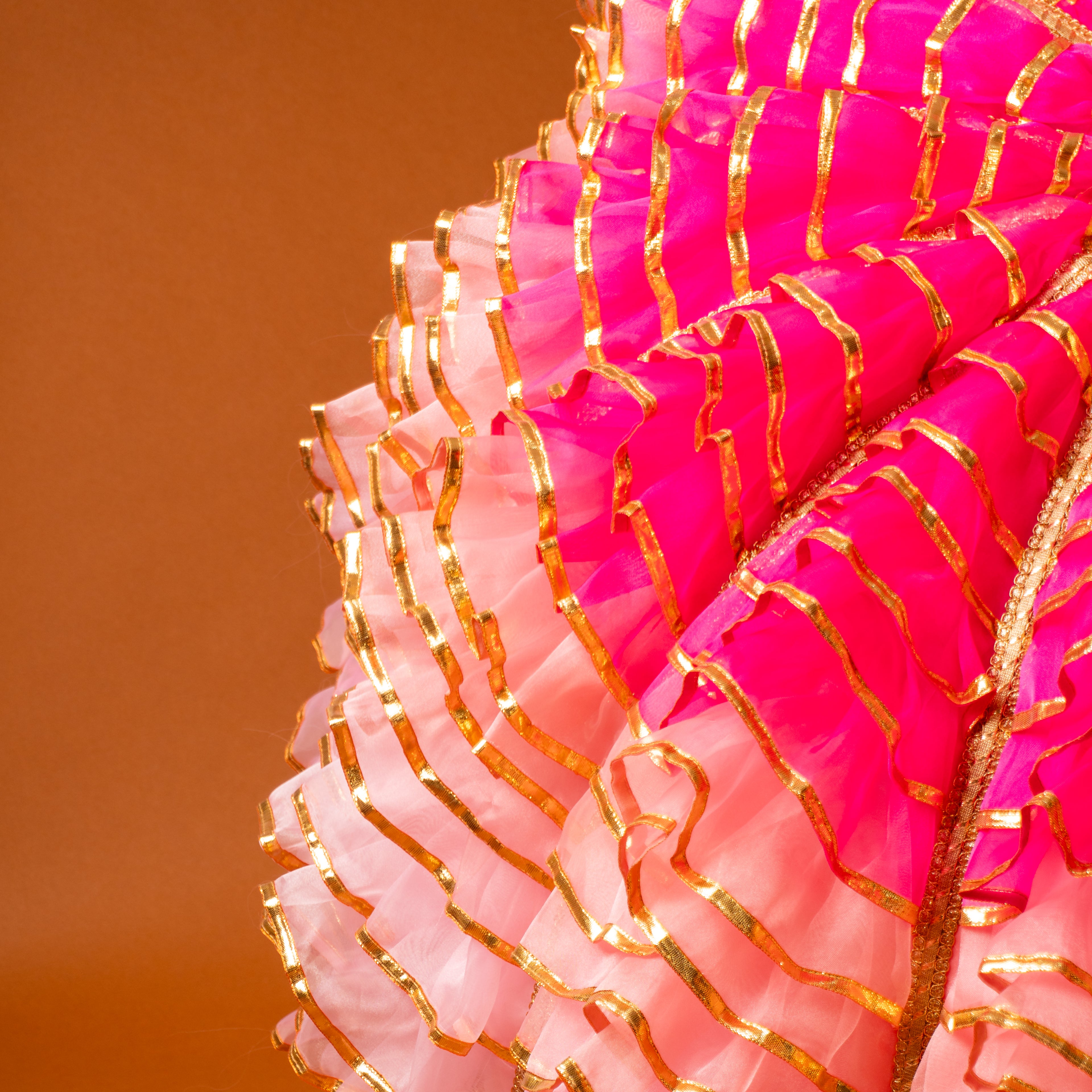 Close-up of pink and gold decorative umbrella with a blurred orange background